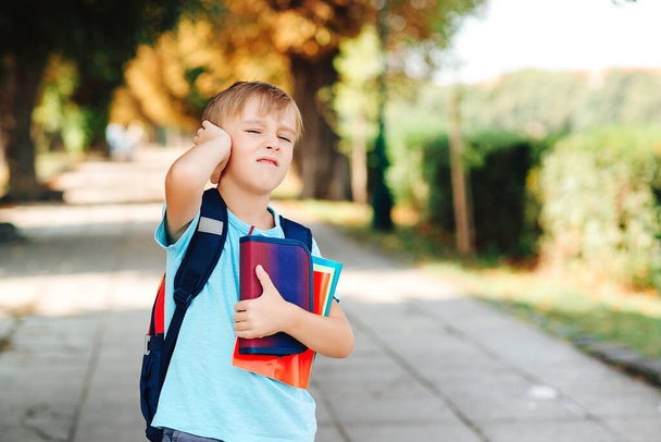 Unhappy school boy with books in hands and backpack. Upset kid going to school. School bullying, depression, stress or frustration. Schoolboy with negative emotions go to school. Education. - Photo, Image