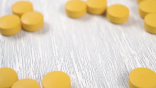 Yellow vitamin tablets spill out from a wooden spoon on a wooden table close up. Macro shot. Selective focus - Footage, Video
