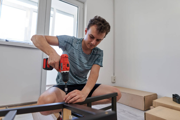 Young man assembling furniture in his new home, new life concept - Foto, Bild