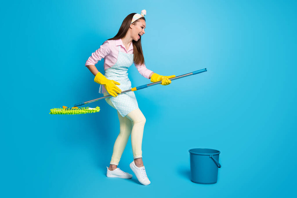 Full size profile photo of attractive funny lady house wife good mood hold mop like cleaning floor wear headband long dotted apron pink shirt pants shoes isolated blue color background - Valokuva, kuva