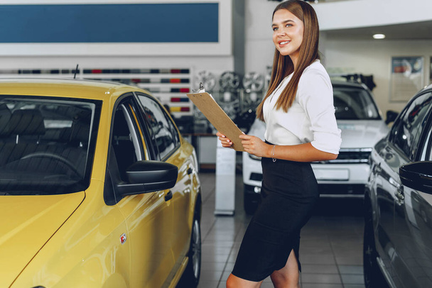 Attractive young female car dealer standing in showroom - Foto, Bild