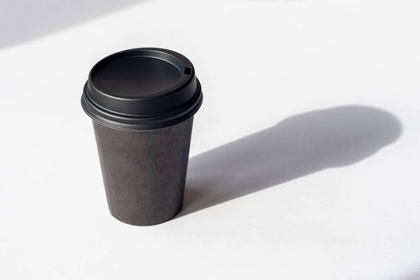 Tasse à café jetable sur table blanche, ombres acérées. - Photo, image