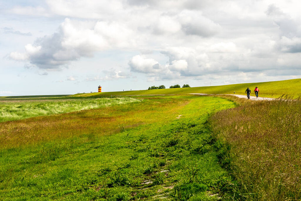 вид на маяк Пилсум в Восточной Фризии с туристами, прогуливающимися вокруг дамбы и фотографирующимися - Фото, изображение