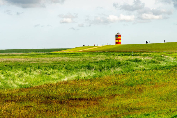 Blick auf den Leuchtturm Pilsum in Ostfriesland mit Touristen, die am Deich spazieren und Fotos machen - Foto, Bild