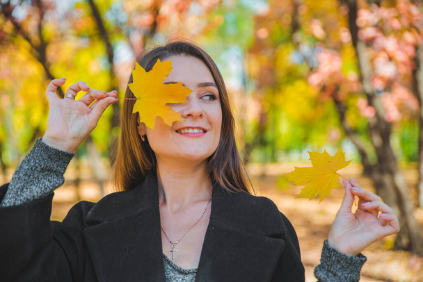 young pretty woman fooling around with yellow maple leaf autumn fashion - Photo, Image