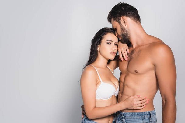 sexy woman in bra touching muscular man standing on grey - Photo, Image