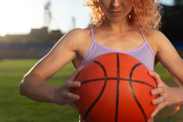 girl athlete biketball player, holding a biketball ball in her hand, against the backdrop of the setting sun.屋外競争力のあるバスケットボール選手がボールを保持-黒の背景に隔離 - 写真・画像