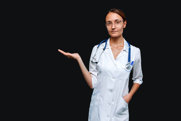 Beautiful female doctor points her palm to the product isolated on gray background - Photo, image