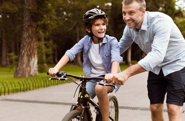 Αγόρι μαθαίνει ποδήλατο με τον ενήλικα πατέρα του. - Φωτογραφία, εικόνα