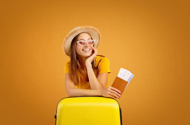 Стильная девушка с паспортом и билетами, опирающаяся на чемодан - Фото, изображение