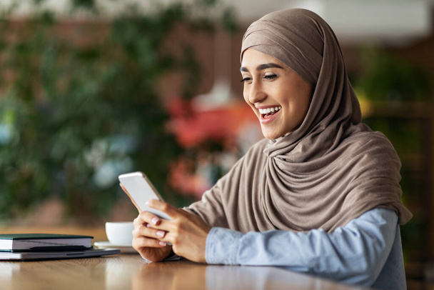 Laughing muslim woman looking at smartphone screen - Фото, изображение