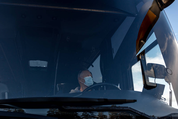 Водитель автобуса в медицинской маске, со стороны лобового окна Безопасное вождение во время пандемии, защита от коронавируса - Фото, изображение