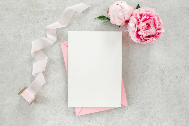 Mockup invitation, blank paper greeting card, pink envelope and peonies on gray stone table. Flower background. Flat lay, top view. - Valokuva, kuva