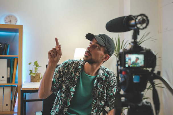 Behind the scene shot of a young man influencer making a video. Very handsome man with beard shooting a video for social media talking directly to the camera. Influencer's amazing work space. - Φωτογραφία, εικόνα