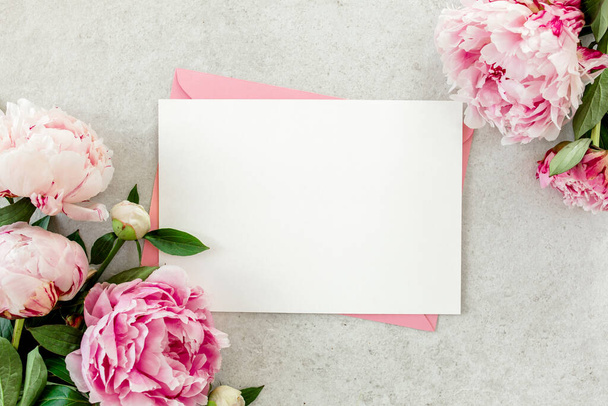 Mockup invitation, blank paper greeting card, pink envelope and peonies on gray stone table. Flower background. Flat lay, top view. - Fotoğraf, Görsel
