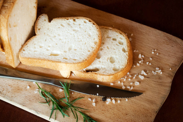 Sliced gluten-free white bread, salt and pepper, herbs on a wooden background. - Photo, Image