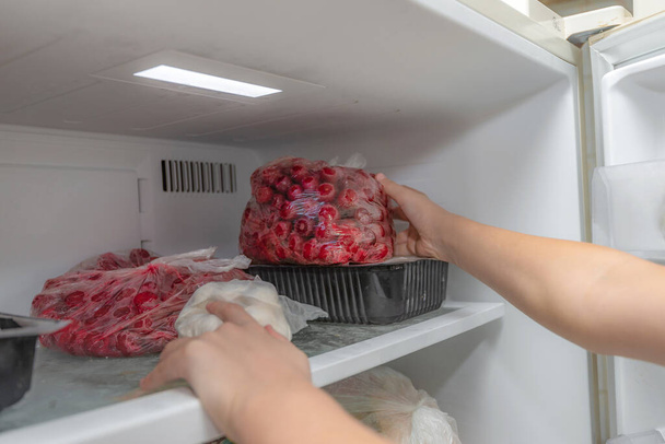 Una mujer pone productos de frutas congeladas en el congelador, para su conservación a largo plazo. - Foto, imagen