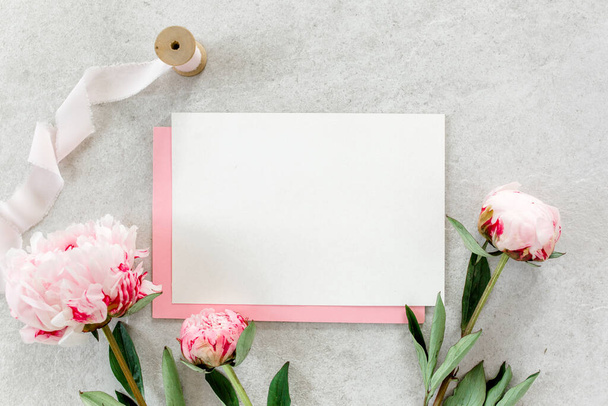 Mockup invitation, blank paper greeting card, pink envelope and peonies on gray stone table. Flower background. Flat lay, top view. - Φωτογραφία, εικόνα