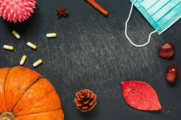 Autumn composition during the coronavirus period. Pumpkin, dried leaves, medical mask, chestnuts, cinnamon, pills on a black background. Autumn, halloween concept. Flat lay, top view, copy space - Φωτογραφία, εικόνα