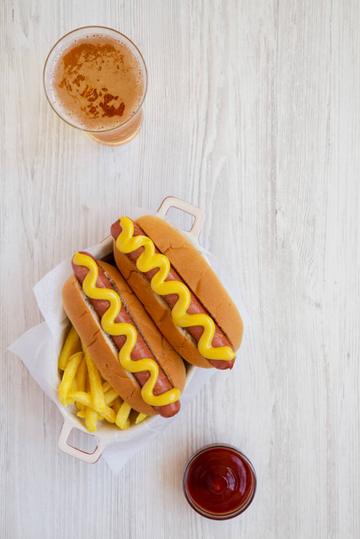 Hot Dog à la moutarde maison avec frites et verre de bière froide sur fond de bois blanc, vue sur le dessus. Couché à plat, au-dessus, par le haut. Espace de copie. - Photo, image
