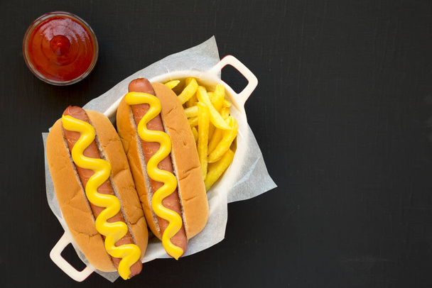 Hot Dog di senape fatta in casa, patatine fritte e vetro di birra su una superficie nera, vista dall'alto. Posa piatta, sopraelevata, dall'alto. Spazio per testo. - Foto, immagini