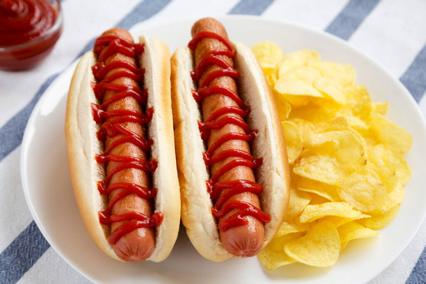 Tasty American Hot Dog with Potato Chips on a white plate, side view. Close-up. - Photo, Image