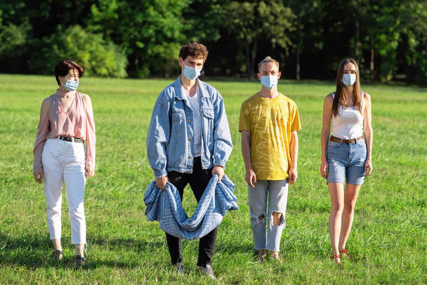 Grupo de amigos con máscaras médicas listos para extender una manta de picnic en un parque durante la pandemia en Chisinau, Moldavia - Foto, Imagen