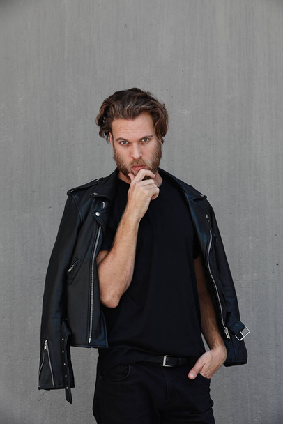 Handsome young bearded man wearing biker leather jacket. Vertical. - Photo, Image