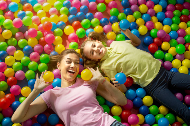 Fun family times. Overhead view of mother with daughter lying in ball pond at indoor amusement park - Foto, Imagem