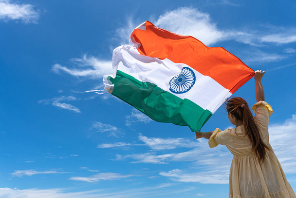 жінка стоїть і тримає прапор Індії під синім небом.. - Фото, зображення