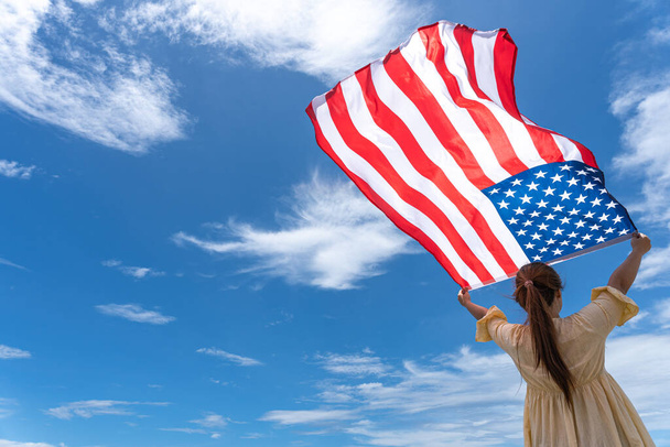 woman standing and holding USA flag under blue sky. - Photo, Image