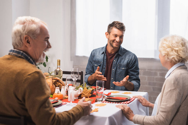 excited man gesturing while talking to senior parents during thanksgiving dinner - 写真・画像