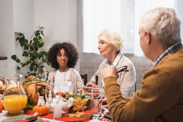 selectieve focus van senior vrouw in gesprek met multiculturele familie tijdens Thanksgiving diner - Foto, afbeelding