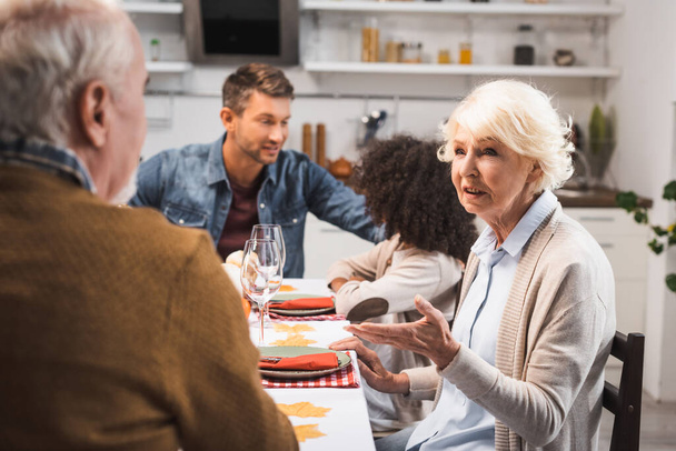 senior woman gesturing while talking during thanksgiving dinner with multicultural family - Φωτογραφία, εικόνα