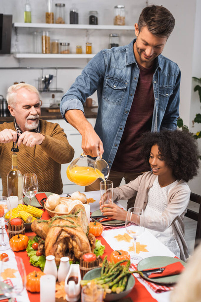 focus selettivo degli uomini che aprono una bottiglia di vino bianco e versano succo d'arancia mentre celebrano il Ringraziamento con famiglia multiculturale - Foto, immagini