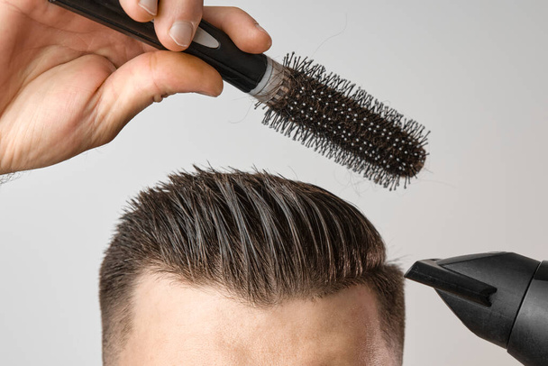 Muž stylizující si vlasy vysoušečem vlasů a kulatým štětcem. Péče o vlasy doma po holičství. Mans móda a moderní sestřih. - Fotografie, Obrázek