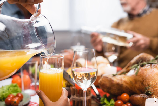 cropped view of african american woman pouring orange juice during thanksgiving dinner - Fotó, kép