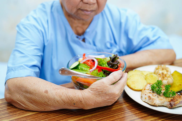 Asiatico anziano o anziano donna anziana paziente mangiare colazione verdura cibo sano con speranza e felice mentre seduto e affamato sul letto in ospedale. - Foto, immagini