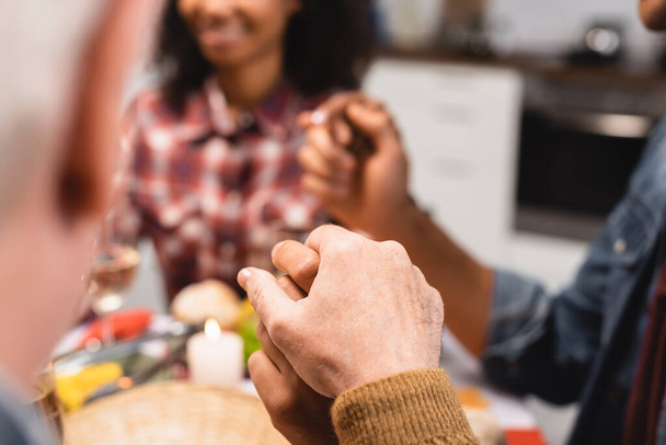 cropped view of interracial family sitting at table and holding hands - Photo, image