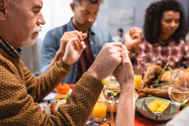selective focus of senior man holding hands with multicultural family on thanksgiving  - Foto, afbeelding