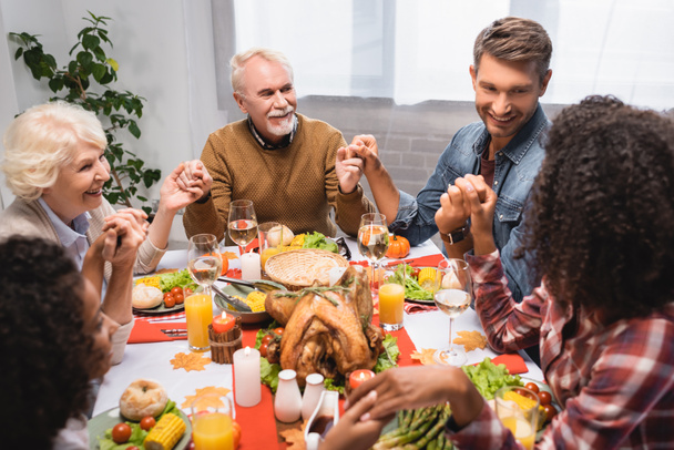 joyful multiethnic family holding hands during dinner on thanksgiving holiday - Photo, Image