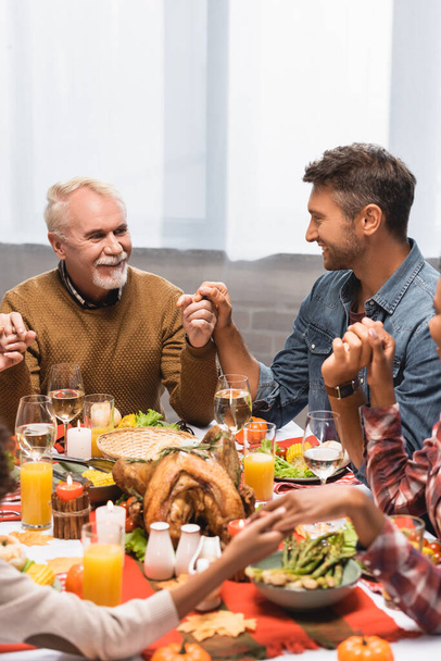 pleased multicultural family holding hands during dinner on thanksgiving holiday - Фото, зображення