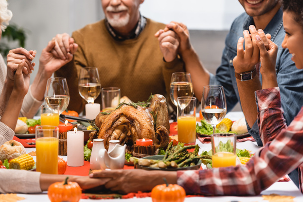 cropped view of pleased multiethnic family holding hands on thanksgiving - Photo, Image