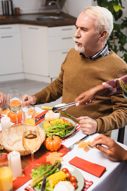 selective focus of african american woman serving vegetables near senior man during thanksgiving dinner - Фото, изображение