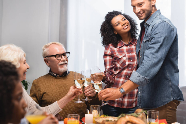 selective focus of multicultural family clinking glasses of white wine while celebrating thanksgiving day - Zdjęcie, obraz