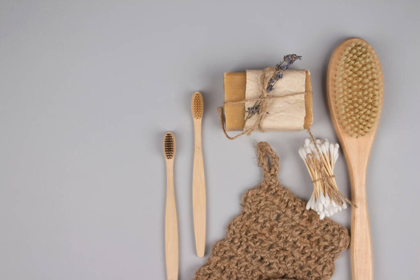 Set of zero waste bathroom essentials on grey background - bamboo toothbrushes, cotton buds, wooden body brush, jute washcloth and organic soap, dry shampoo - home spa concept, mockup and copyspace - Fotó, kép