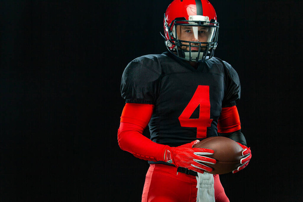 American football player, athlete sportsman in red helmet on black background. Sport and motivation wallpaper. - Foto, Imagen