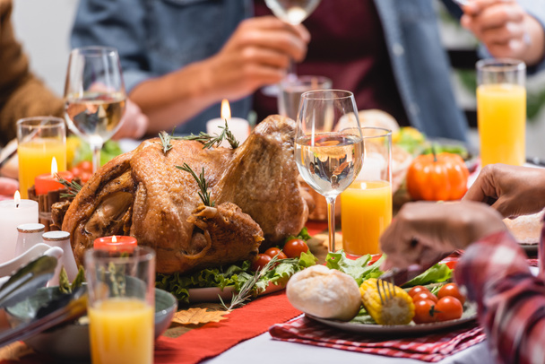 Cropped view of turkey with drinks and candles on table near multiethnic family celebrating thanksgiving  - 写真・画像