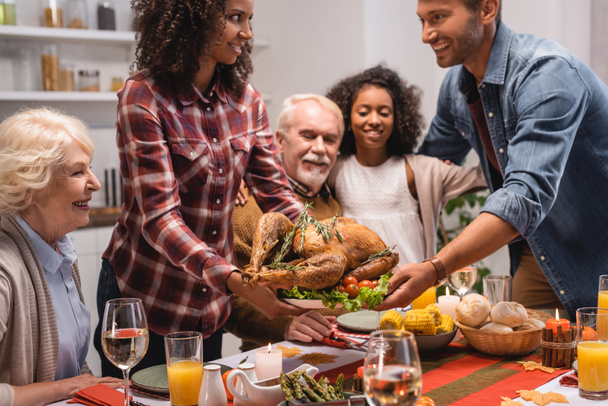 Selective focus of african american woman giving turkey to husband near family during thanksgiving dinner  - Fotoğraf, Görsel