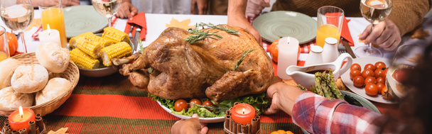 Horizontal image of african american woman putting turkey on table near family during thanksgiving dinner  - Fotó, kép